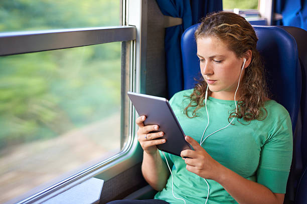 Shot of a young woman using her digital tablet and listening to music while on a train journey
